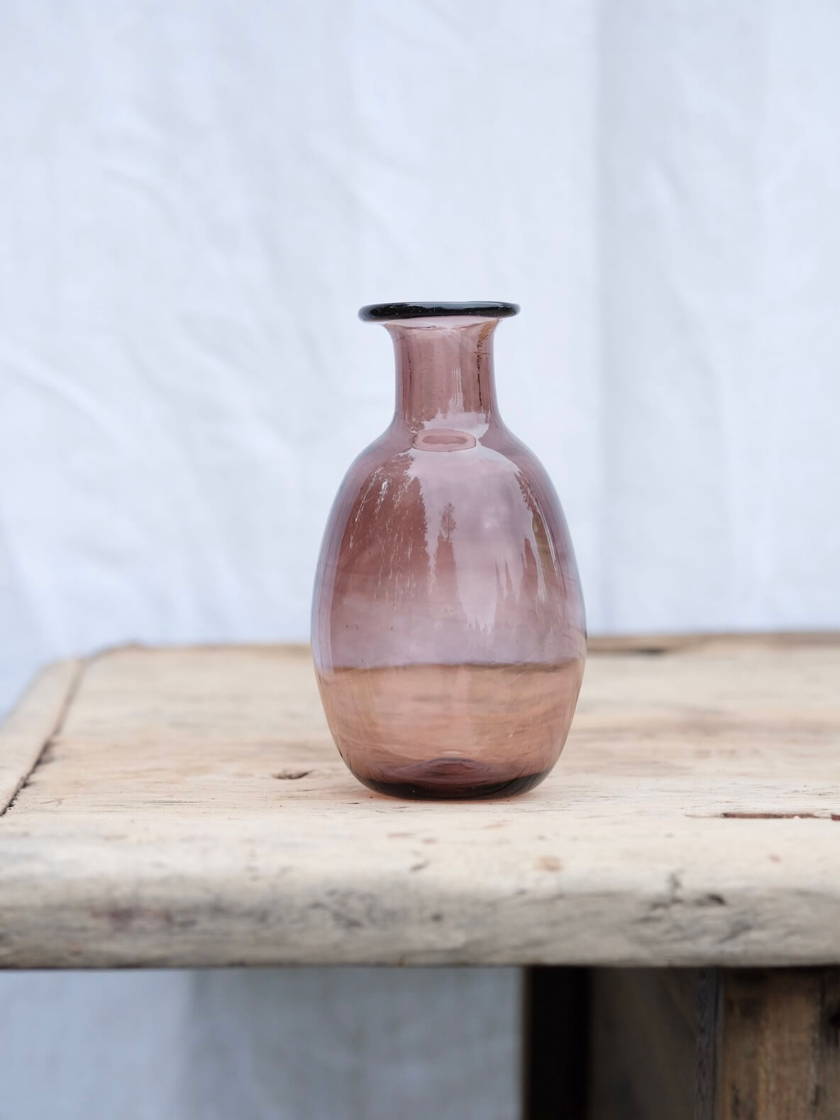 Small raspberry coloured vase sitting on a vintage wooden table. Handblown in Paris by La Soufflerie.
