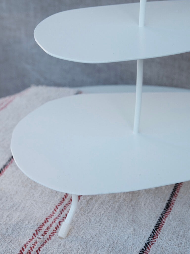 close up of the base of the white etagere. It shows the largest of the three trays that is on the bottom as well as one of thes small feet its stands on.