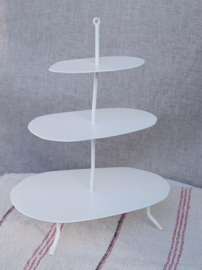 white etagere used for serving food. It has three seperate levels attached in the middle by a piece of wonky metal.