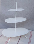 white etagere used for serving food. It has three seperate levels attached in the middle by a piece of wonky metal.