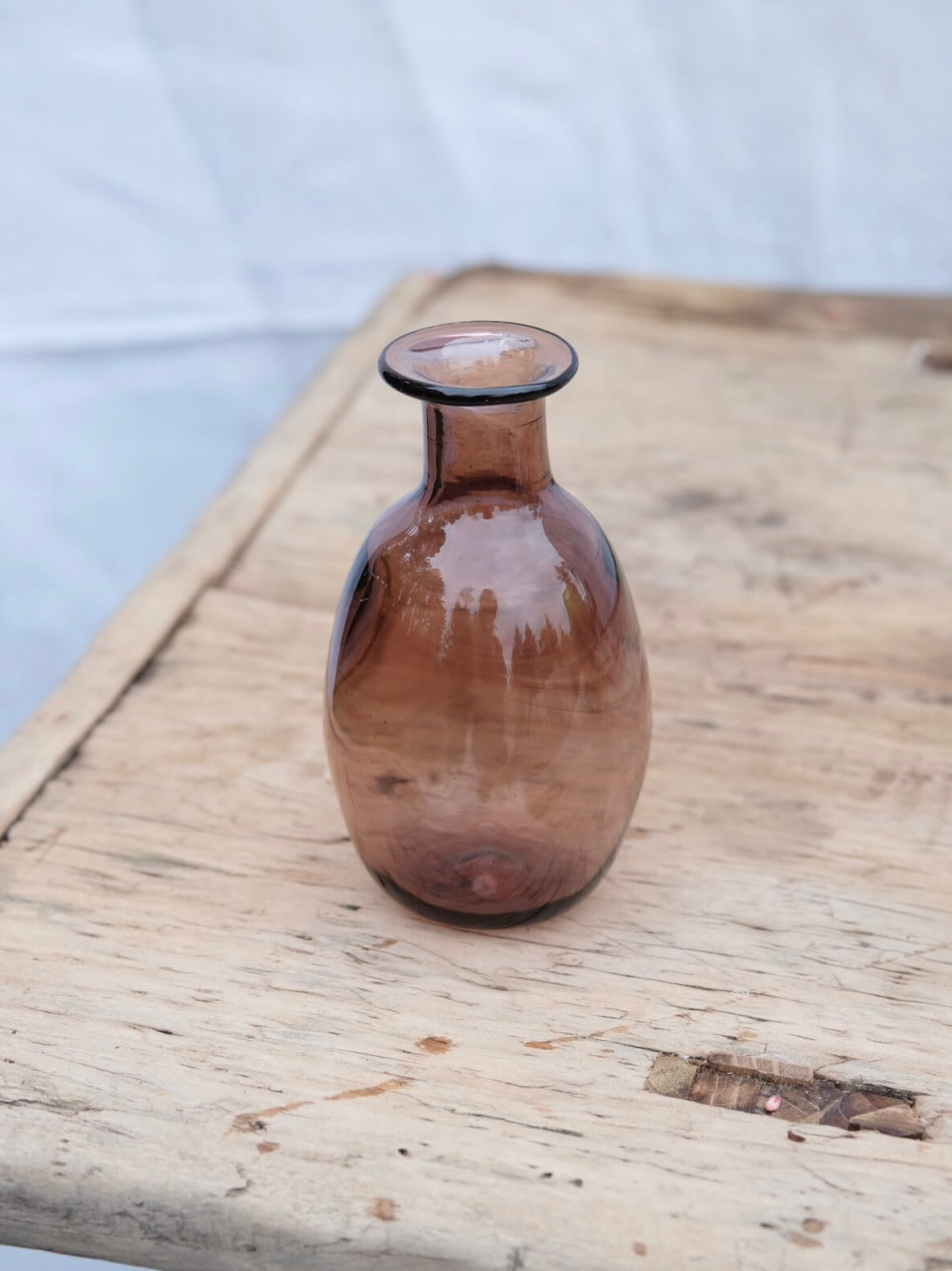 Small raspberry coloured vase sitting on a vintage wooden table. Handblown in Paris by La Soufflerie.